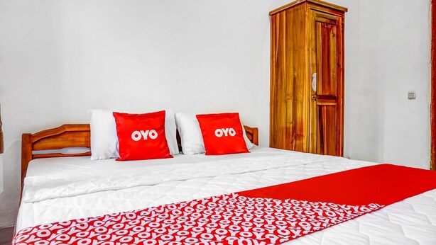 A bed with white and red bedding, a wooden wardrobe, and a red and white patterned bedspread. - OYO 90846 Guesthouse Bintaro Asri Syariah (South Tangerang)