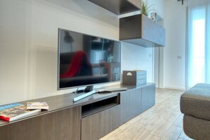 A modern living room with a flat-screen TV mounted on a wooden entertainment unit, a grey sofa, and a small plant on a shelf. - CaseOspitali - Casa Francesca modernissimo trilo (Pioltello)