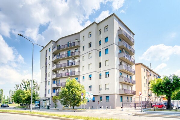 A multi-story residential building with balconies, a bus stop, and a clear sky.