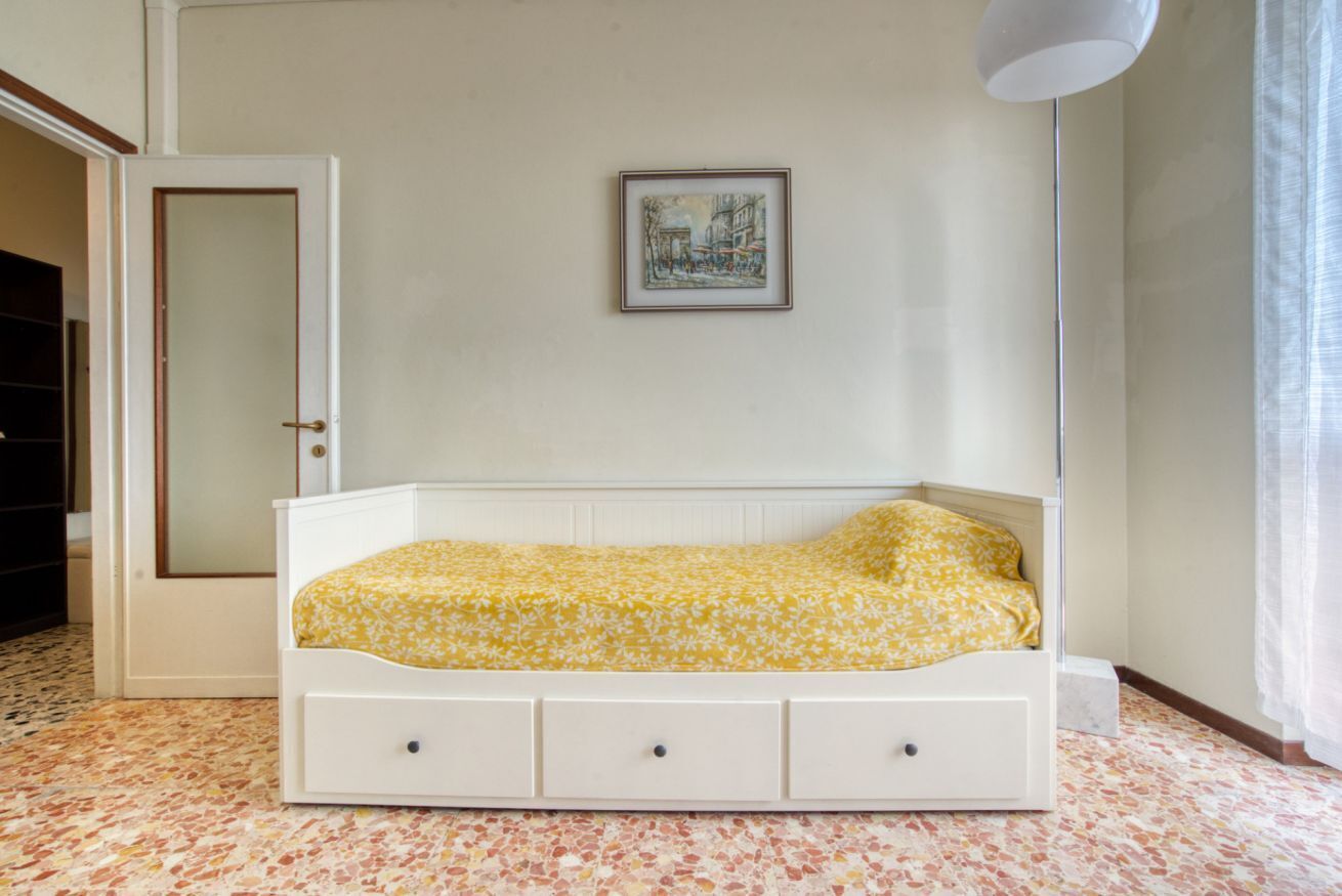 A bedroom with a bed, a door, a framed picture on the wall, and a light fixture.