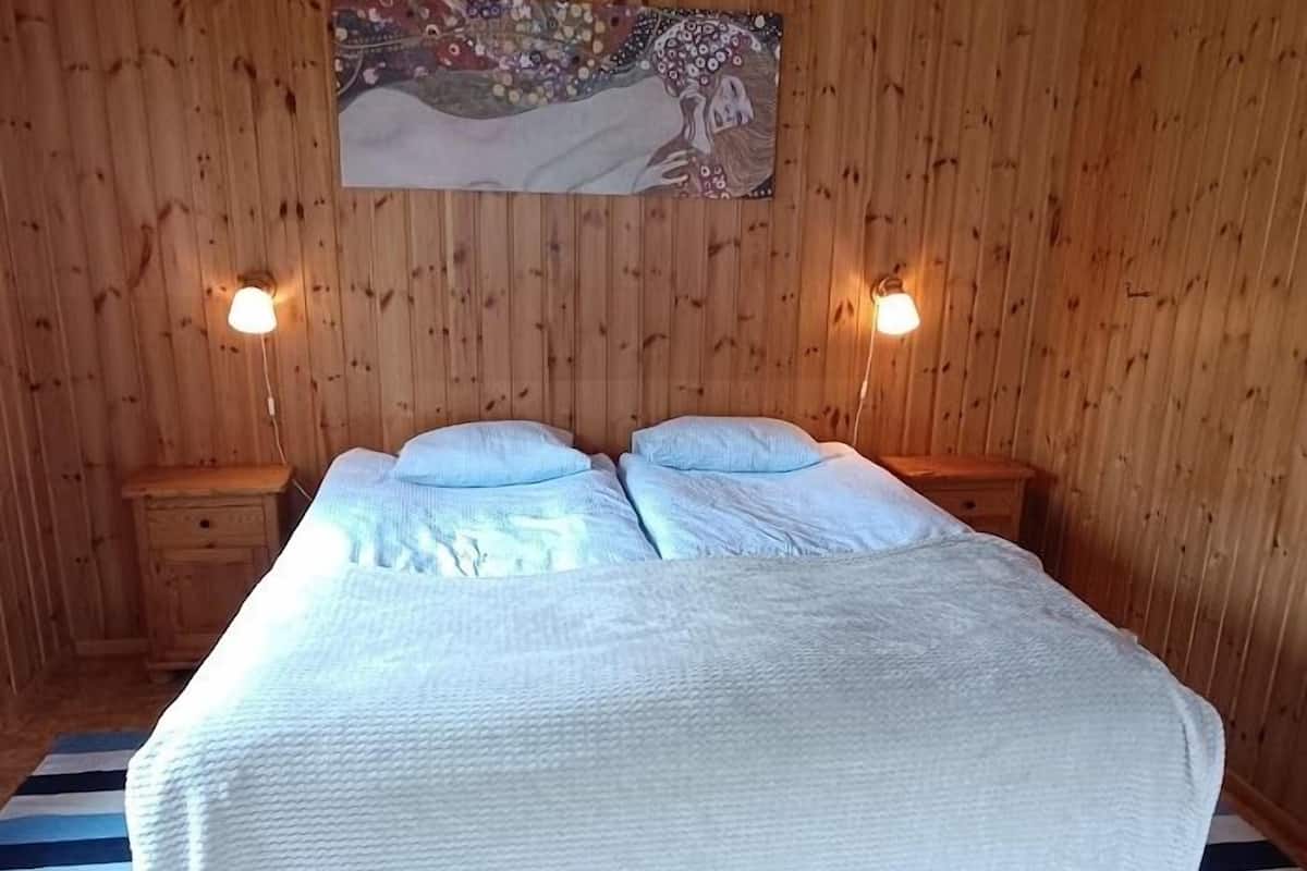 A wooden-paneled room with a bed, two bedside tables, and a wall-mounted painting.