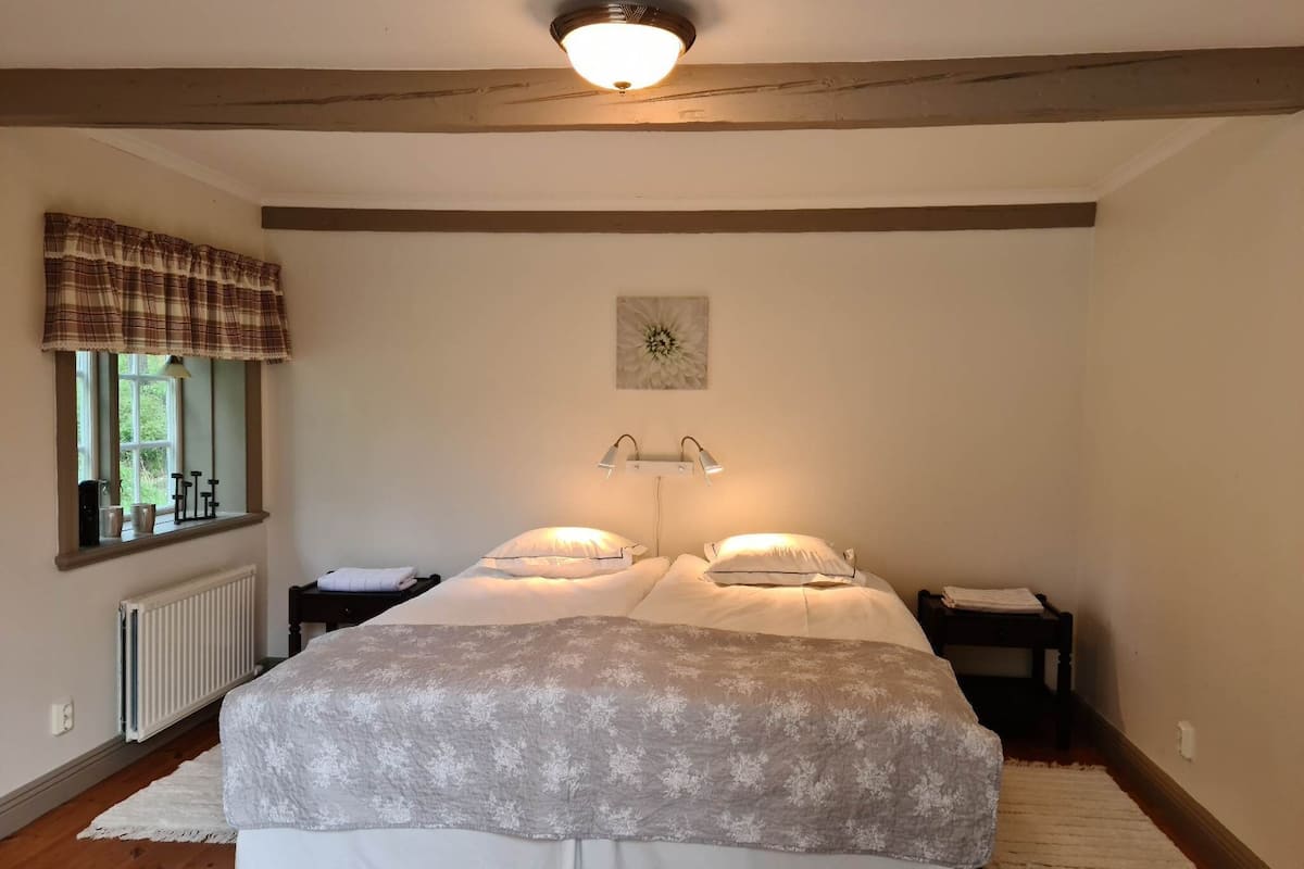A bedroom with a double bed, two bedside tables, a window with curtains, a radiator, and a ceiling light fixture.
