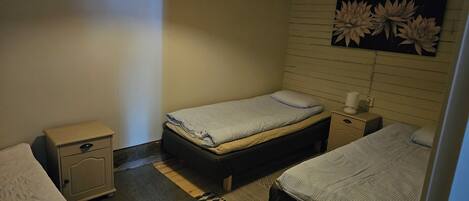 A small, dimly lit room with a single bed, a nightstand, and a wall-mounted flower decoration.