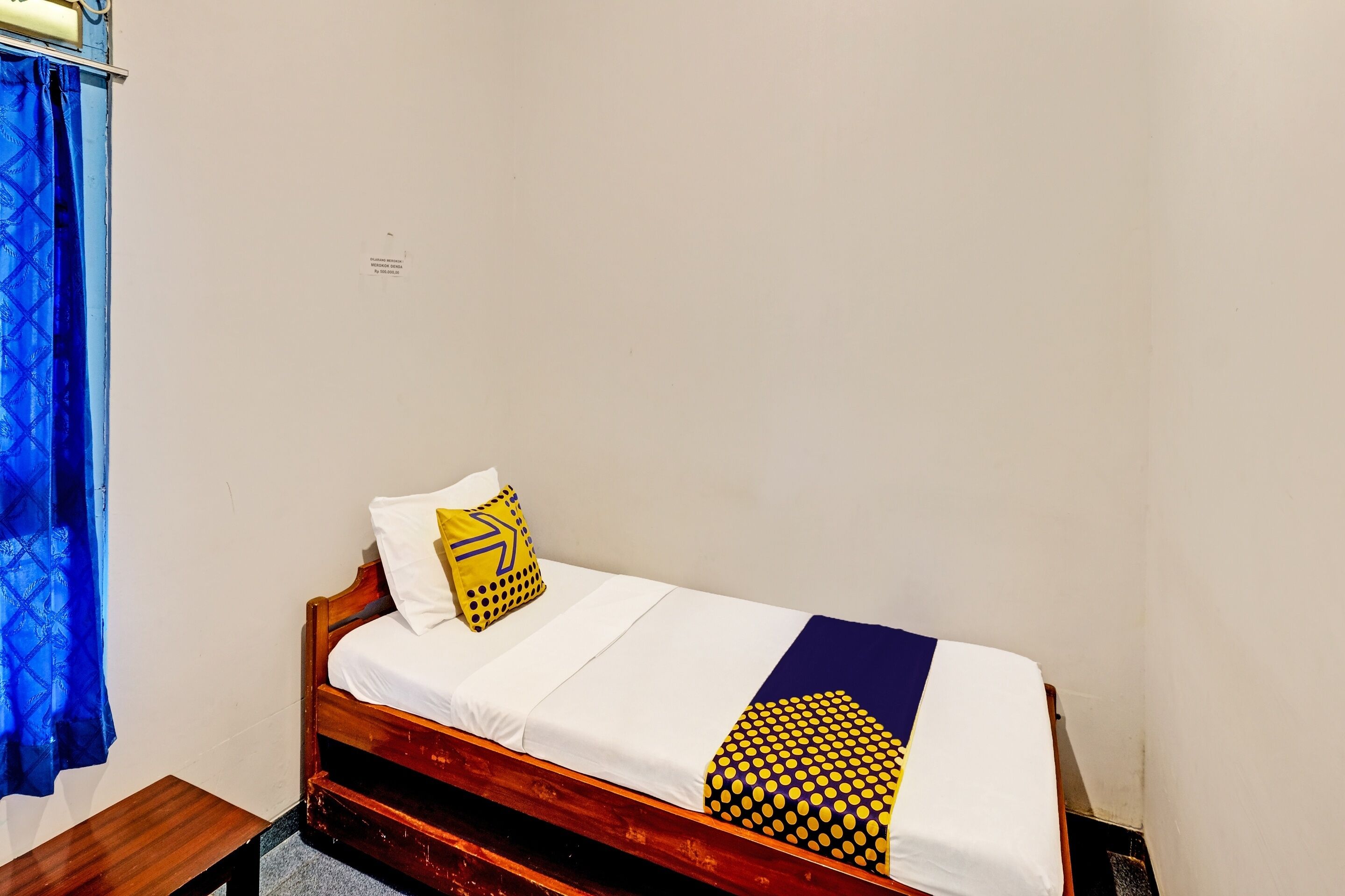 A single bed with a wooden frame, white bedding, and a blue and yellow patterned pillow.