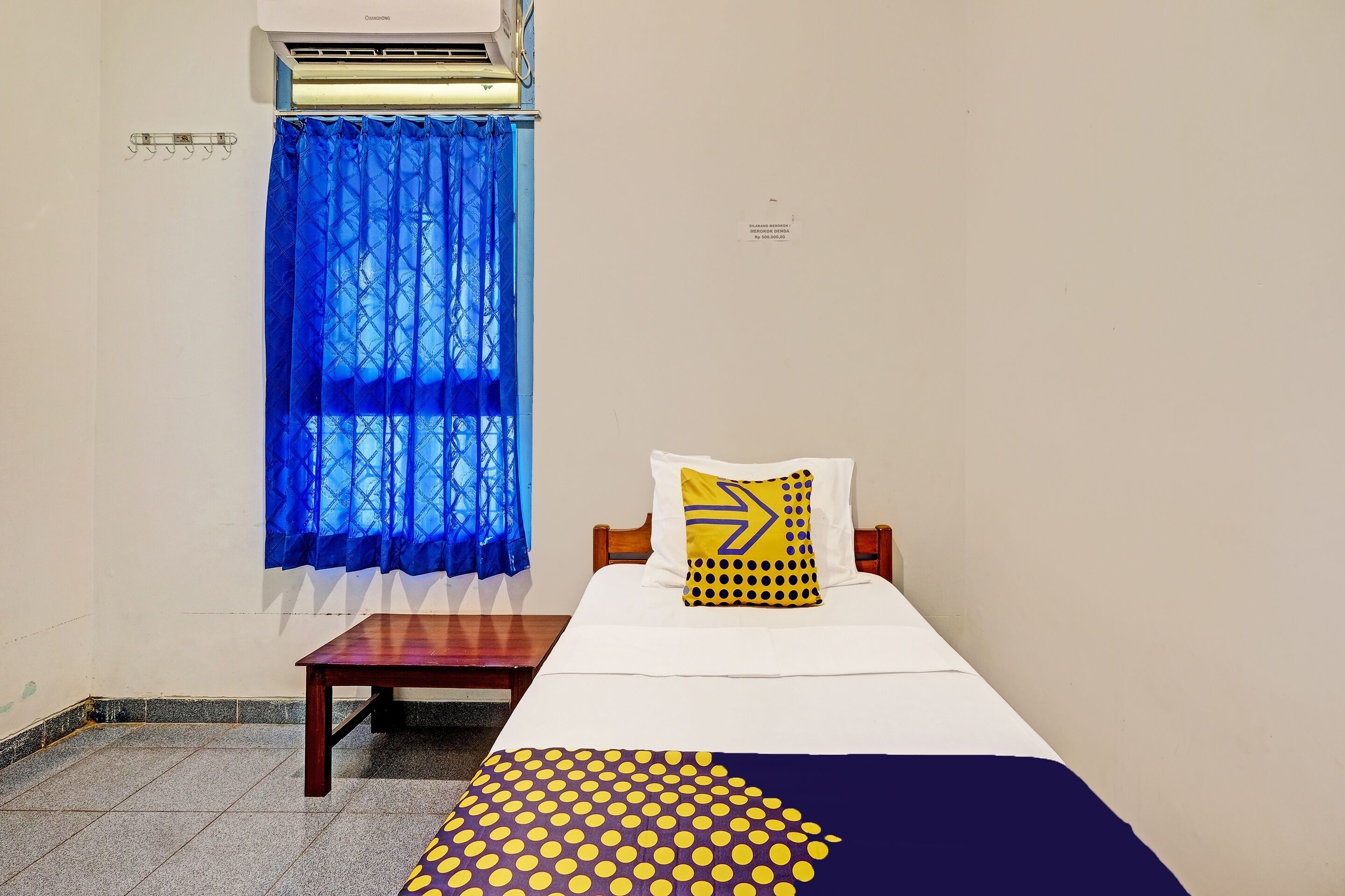 Une chambre à coucher avec un lit, une table de chevet en bois, un rideau bleu et un appareil de climatisation.