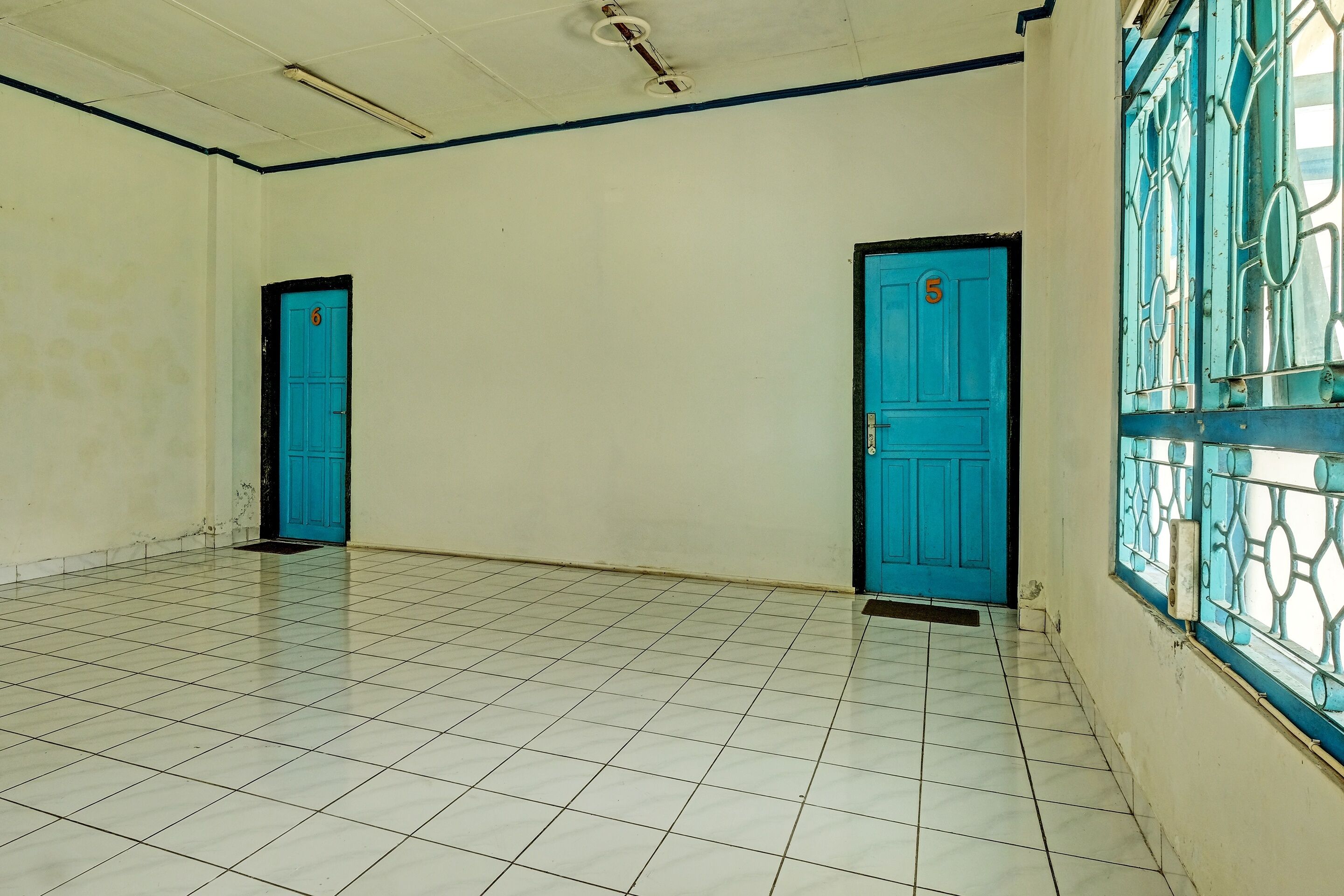 A hallway with two blue doors, white tiled floor, and a window with decorative metal bars.