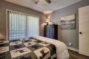 A bedroom with a bed, a nightstand, a lamp, a painting, and a door.