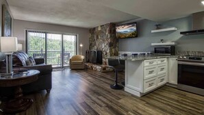 A spacious living area with a stone accent wall, a large window, and a kitchen with white cabinetry and a built-in oven.