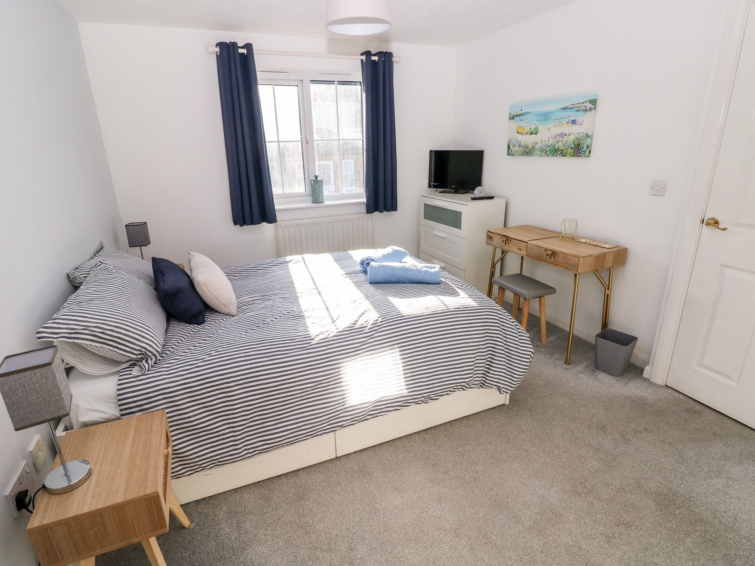 A bedroom with a bed, a desk, a TV, and a painting on the wall.