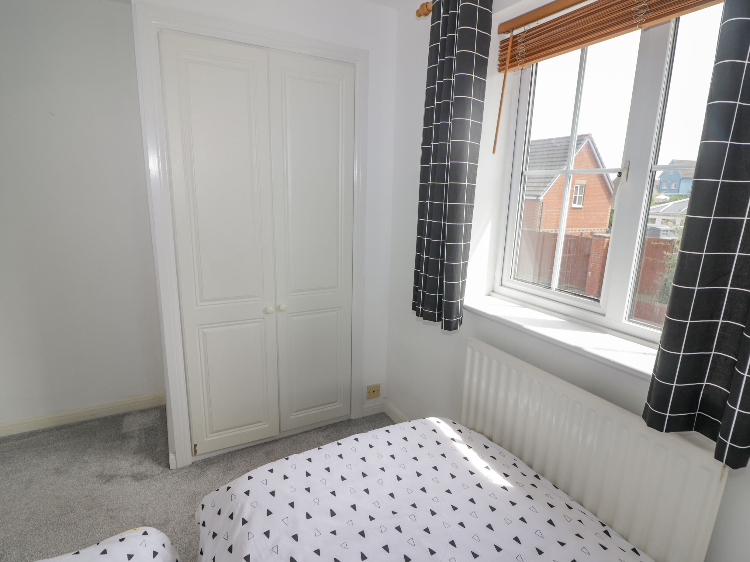 A bedroom with a bed, a white wardrobe, a window with curtains, and a radiator.