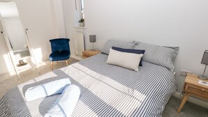 Un dormitorio con cama, una silla, una mesita de noche, una lámpara y una ventana con una planta.