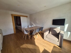Un soggiorno moderno con un tavolo da pranzo in legno, sedie grigie, un divano grigio e una TV a parete.