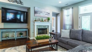 Een woonkamer met een flatscreen televisie, open haard, bank en een decoratieve plank met planten.