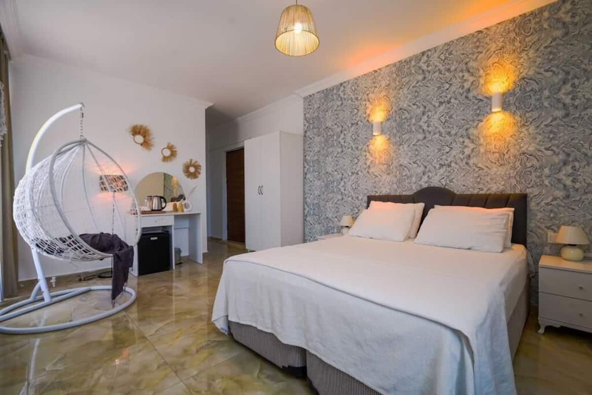 A bedroom with a large bed, a hanging chair, a desk, and a wall-mounted light fixture.