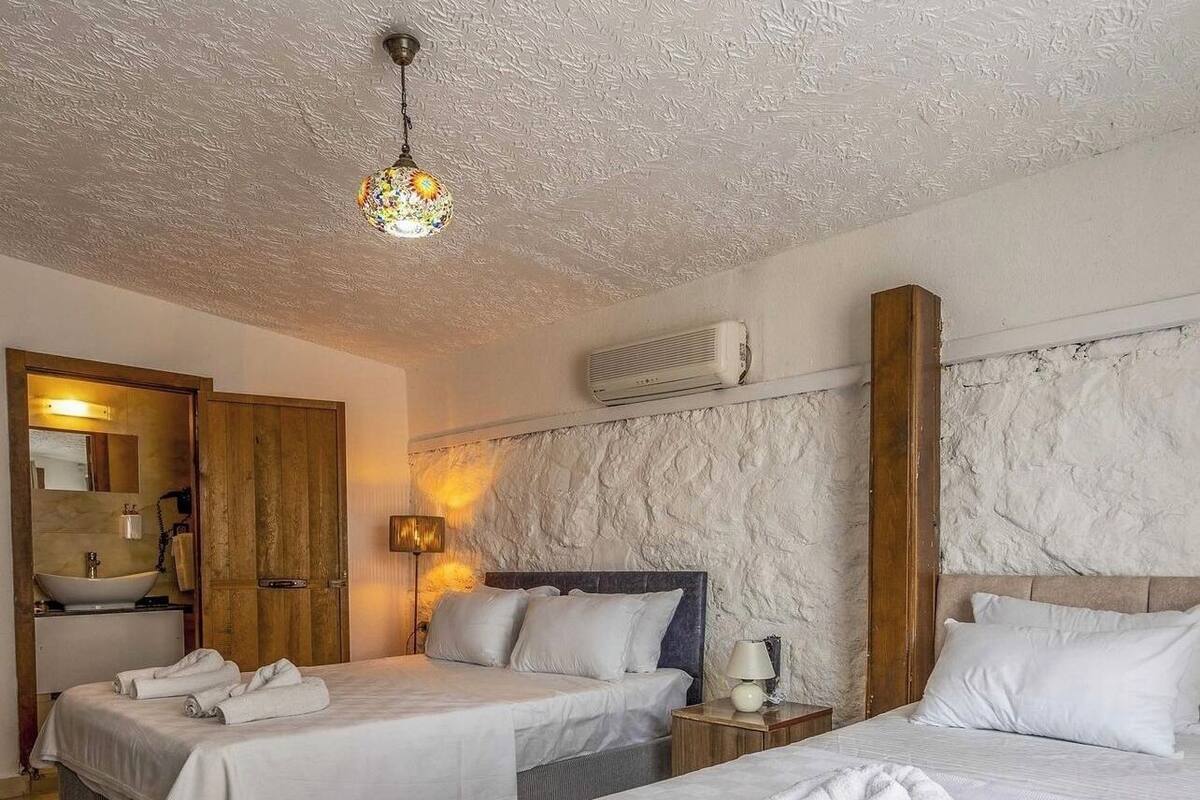 A hotel room with two beds, a wooden wardrobe, a bathroom with a sink, and a textured wall.