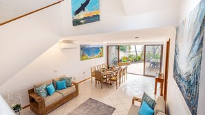A spacious living area with a dining table set for six, a sofa with cushions, and a large painting of a bird.