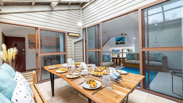 A dining area with a wooden table set for breakfast, large sliding glass doors leading to a pool, and a view of the backyard.