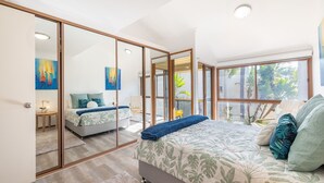A bedroom with a large bed, a sliding glass door leading to a balcony, and artwork on the walls.