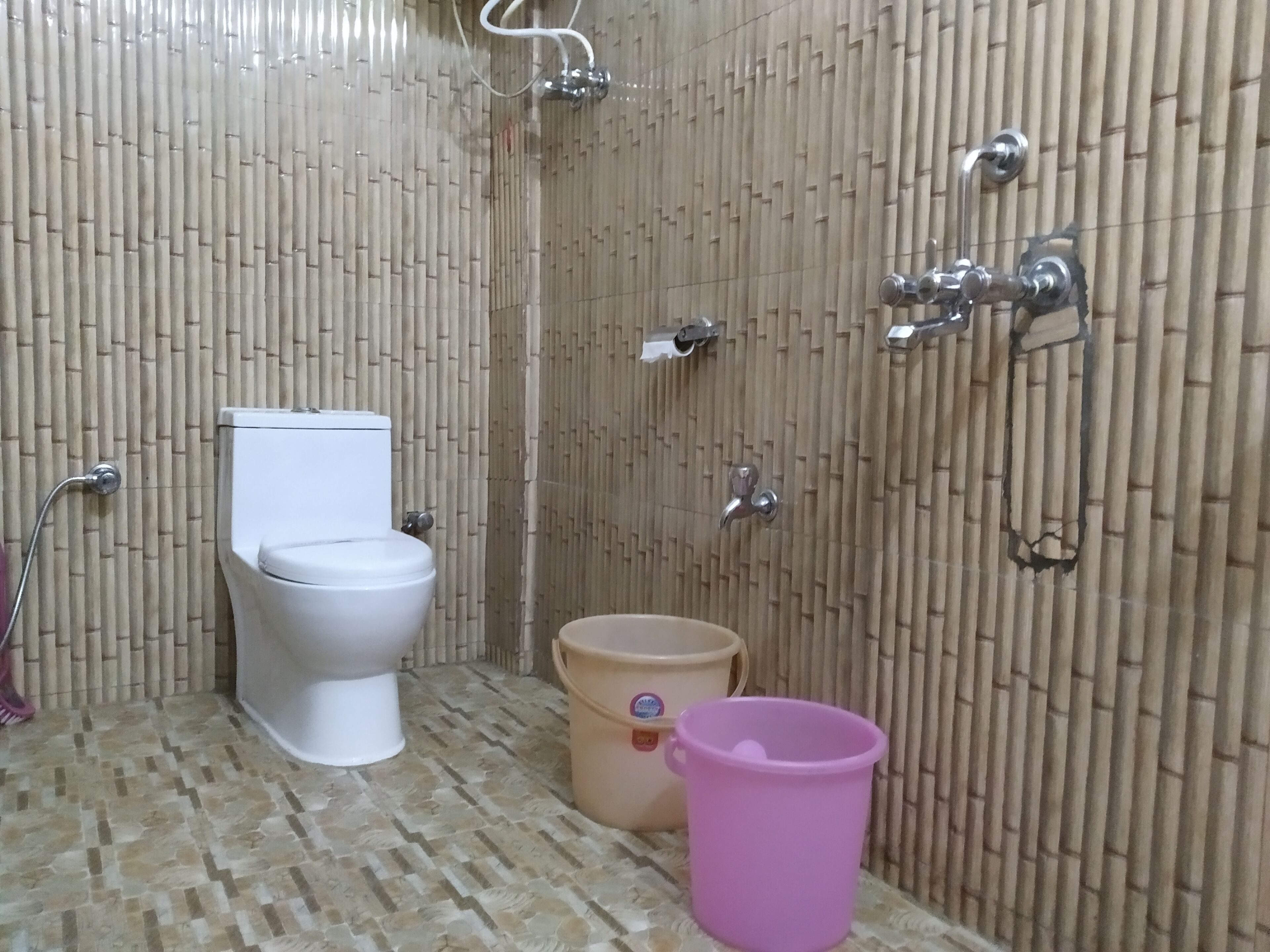 A bathroom with a toilet, a shower, and a bucket on the floor.