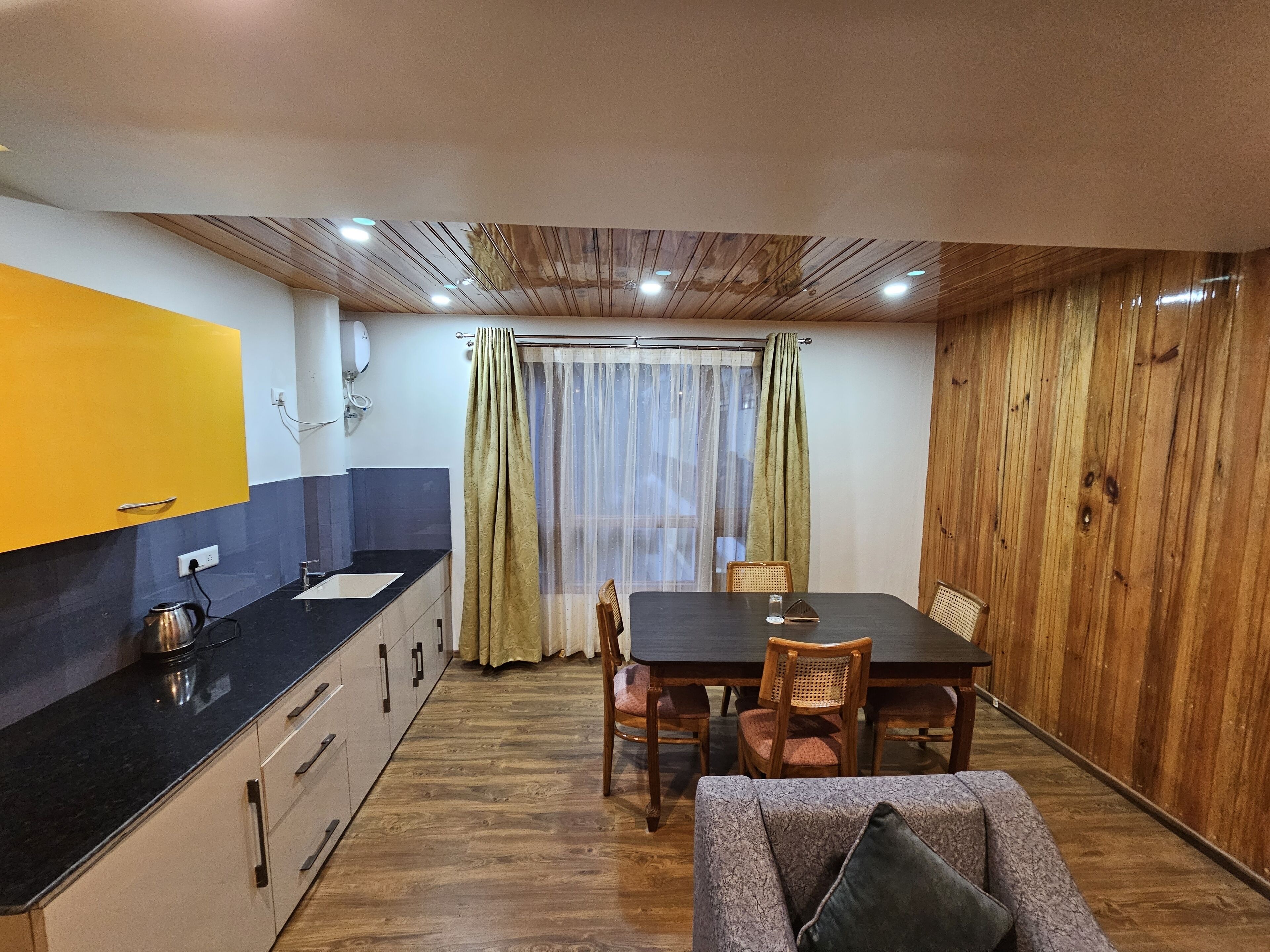 A compact kitchen with a black countertop, wooden cabinets, and a dining area with a table and chairs.