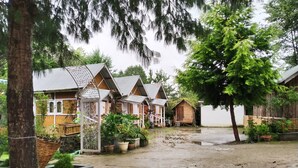 Une rangée de cabanes en bois, avec un sol en terre battue et des plantes en pot.
