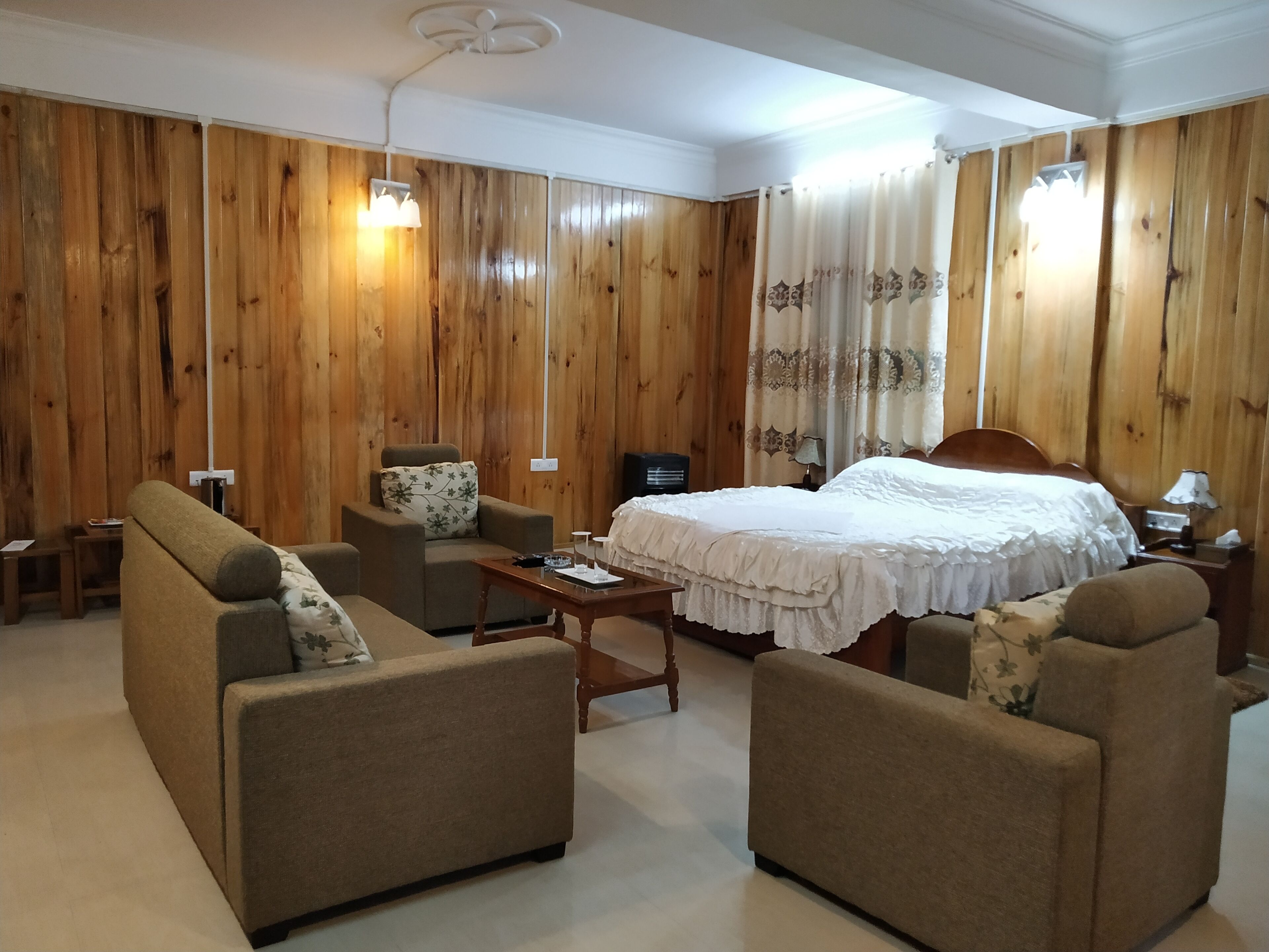 Una habitación con una cama, dos sofás, una mesita y paneles de madera en las paredes.