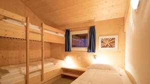 Una habitación de cabaña de madera con literas, una ventana con cortinas y un cuadro en la pared.