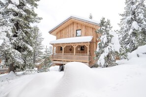 Surrounded by snow-covered trees, this cabin offers a peaceful retreat with a spacious balcony and a cozy front porch.