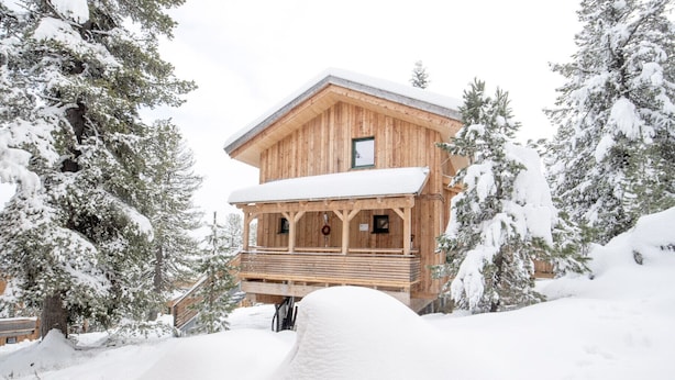 Una cabaña de madera con balcón, rodeada de árboles cubiertos de nieve.