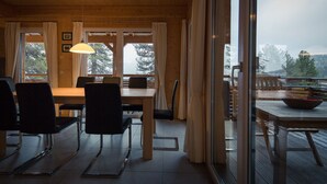 Un interior de madera con zona de comedor, ventanas amplias y vistas a un paisaje boscoso.