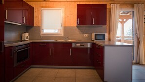 Cocina compacta con gabinetes rojos, horno integrado, microondas y ventana sobre el fregadero.