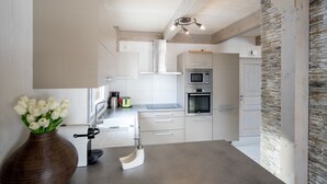 A modern kitchen with white cabinetry, a stone accent wall, and a wooden ceiling.