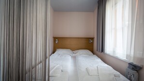 Ein Einzelbett mit Holz-Kopfteil in einem Zimmer mit Fenster und leichtem Vorhang.