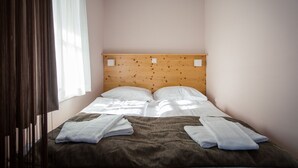 Un lit simple avec une tête de lit en bois, une literie blanche et deux serviettes pliées posées sur le lit.