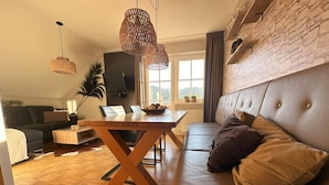 A modern living room with a sofa, a dining table, and hanging wicker lamps. - Apartment # 14 with balcony (Turrach)