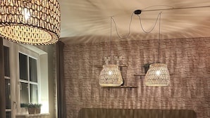 A dining area with a stone wall, wooden table, and chairs. There are two hanging lights and a radiator near the window. - Apartment # 14 with balcony (Turrach)