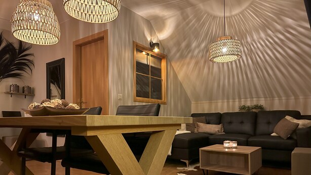 A modern living room with a wooden dining table, a black sofa, and a unique ceiling design. - Apartment # 14 with balcony (Turrach)