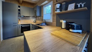 Une cuisine moderne avec des meubles en bois, un four encastré, un évier et une machine à café posée sur une étagère.