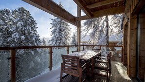Une terrasse en bois avec une table et des chaises, donnant sur un paysage enneigé parsemé d’arbres.