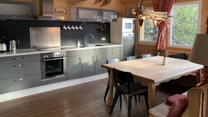 Une cuisine moderne avec des meubles gris, des appareils en acier inoxydable et une table à manger en bois, accompagnée de chaises.