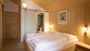 Une pièce aux murs lambrissés, avec un lit double, une petite table de chevet, une lampe fixée au mur et une affiche représentant un skieur.