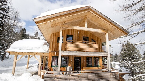 Un chalet en bois doté d’un balcon, de nombreuses fenêtres et d’un toit recouvert de neige.