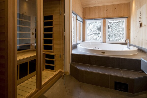 A modern bathroom with a freestanding bathtub, a walk-in shower, and a view of snow-covered trees through large windows.