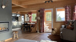 Un intérieur de chalet chaleureux avec une cheminée, une table à manger en bois et un coin salon confortable.