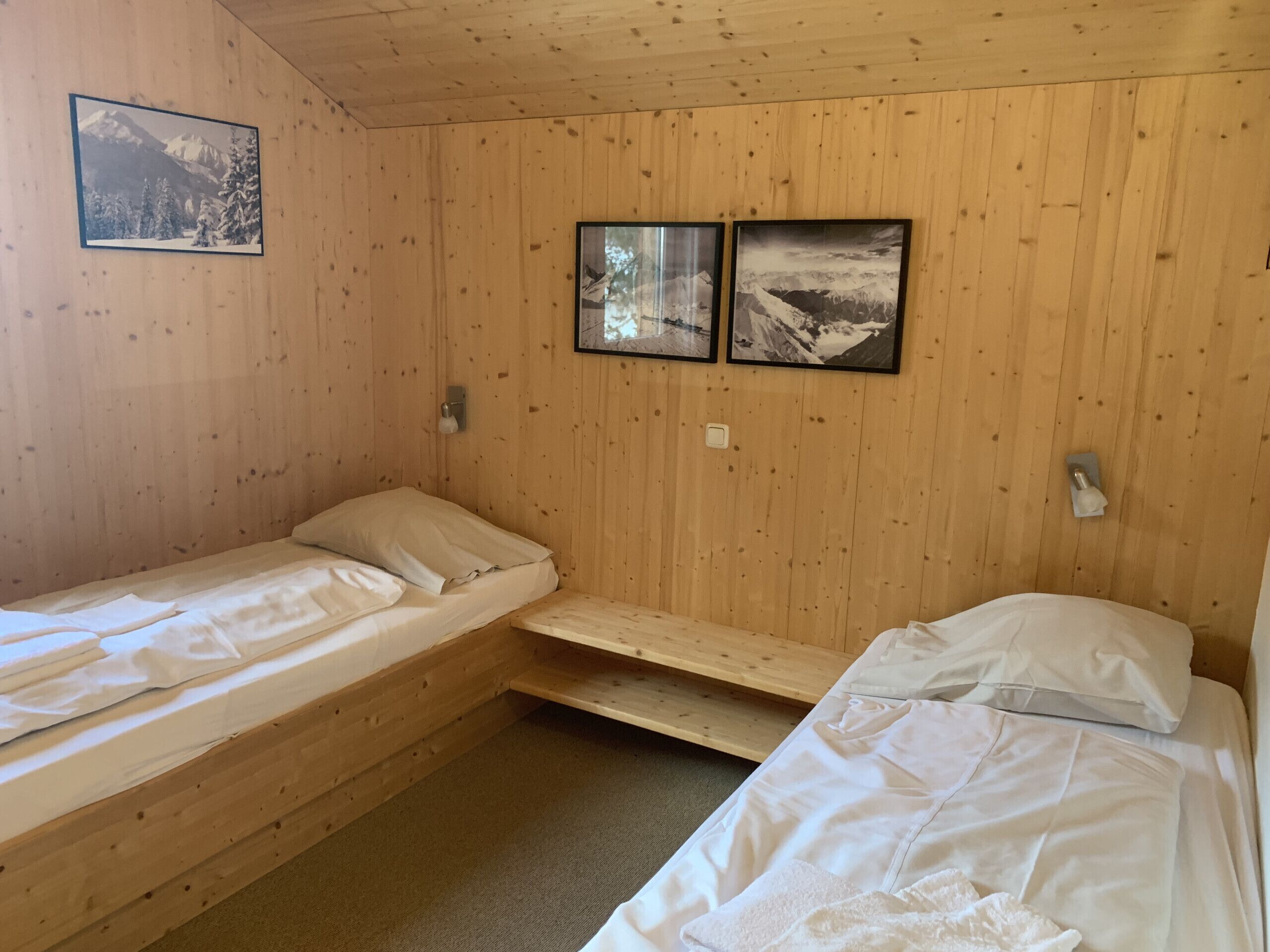 A cabin-style room with two single beds, wooden walls, and two framed pictures depicting snowy landscapes.