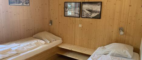A cabin-style room with two single beds, wooden walls, and two framed pictures depicting snowy landscapes.