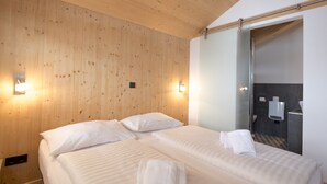 Ein Hotelzimmer mit zwei Betten, Holzwänden und einem durch eine Glastür sichtbaren Badezimmer.