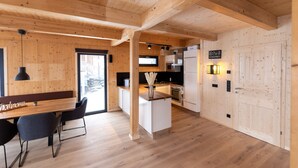 Eine moderne Küche mit Holzbalken, einem Essbereich mit Holztisch und -stühlen sowie einem großen Fenster.