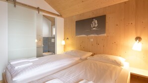 A hotel room with a wooden ceiling, a bed with white linens, a shower area, and a painting on the wall. - Chalet #16 with IR-sauna and indoor whirlpool (Turrach)