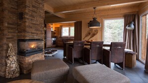 A cozy cabin interior with a stone fireplace, wooden dining area, and large windows. - Chalet #16 with IR-sauna and indoor whirlpool (Turrach)